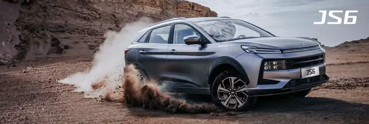 SUV JS6 derrapando en terreno rocoso con montaña de fondo.